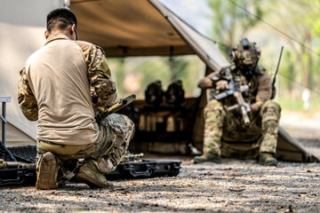 Special forces soldiers preparing tactical gear at military field base camp with weapons and...