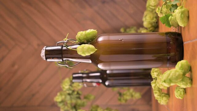Macro shot of a cold brown beer bottle with a droplet of condensation slowly sliding down. Fresh green hops decorate the bottle. Symbol of refreshment, thirst, and artisanal brewing. High 4k footage