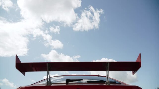 Rear sports spoiler of racing car against background of sky with clouds. Additional parts and upgrade of stock coupe for better handling. Tuning and parts for its implementation.