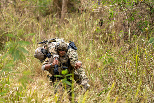 Special forces soldier carrying injured comrade on his shoulders through tall grass during jungle rescue drill. Courage, teamwork, and battlefield emergency training depicted.