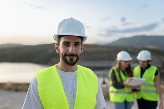 Young male engineer smiling at camera with colleagues working in background