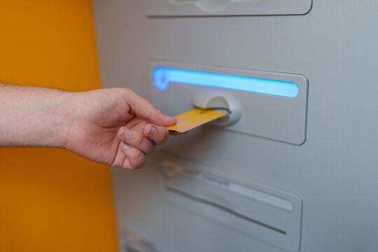 Yellow credit card being inserted into ATM machine, performing secure bank transaction against vibrant orange backdrop