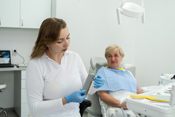 Caucasian fremale dentist with woman patient choose teeth color shades guide for tooth whitening in...