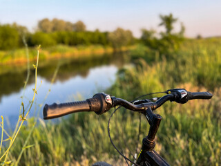 Bicycle handlebar overlooking tranquil river during sunset, inviting exploration of nature