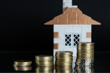 Coins stacked in a column with the dynamics of savings growth against the background of a house....