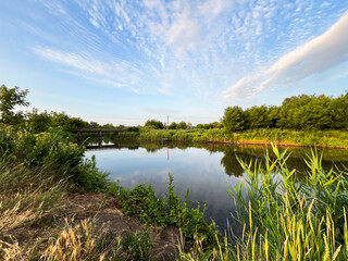 Small wooden bridge crossing calm river at sunset with cloudy sky