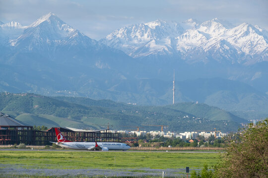Almaty, Kazakhstan - May 25, 2025: Turkish Airlines passenger airplane taxiing on runway with Kok Tobe TV tower and snow-capped mountain backdrop at Almaty International Airport.