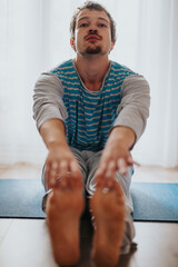 Young man performing flexibility exercises, nearing his toes with arms extended while seated on a...
