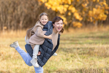 Fototapeta premium Loving mother holds her little daughter in her arms during a peaceful autumn walk in the park, surrounded by vibrant fall foliage. Warmth and affection moment, capturing the beauty of family bonding