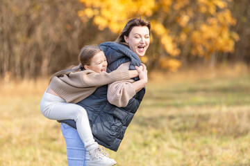 Fototapeta premium Loving mother holds her little daughter in her arms during a peaceful autumn walk in the park, surrounded by vibrant fall foliage. Warmth and affection moment, capturing the beauty of family bonding