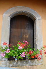 A bright red geranium in a clay pot in a window framed by a beautiful. weathered, thick stone wall.