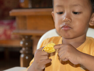 Close up of Toddler eating toast. Happy Asian toddler boy is having breakfast of toast with cheese and egg on his high chair. Toddler boy is having breakfast of toast on his high chair and table.
