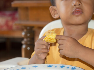 Close up of Toddler eating toast. Happy Asian toddler boy is having breakfast of toast with cheese and egg on his high chair. Toddler boy is having breakfast of toast on his high chair and table.