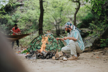 Fototapeta premium Men engage in outdoor camping, with one tending a campfire in a serene forest. A tent and hammock complement the natural surroundings, representing adventure, relaxation, and communion with nature.