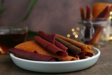 Tasty fruit leather rolls on wooden table, closeup. Space for text