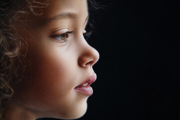 Fototapeta premium Close-Up of a Young Girl's Face with Curly Hair and Soft Makeup Against Black Background