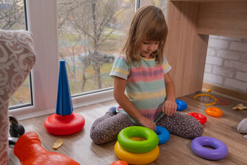 Child plays on the floor with colorful toys in cozy living room by the window