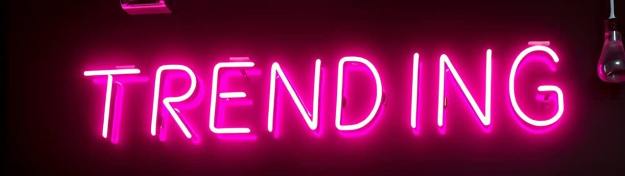 Neon pink neon sign with the word trending in a dark room