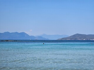 A beautiful view of the coast from a beach on an island in Greece, overlooking mountains and crystal clear water.
