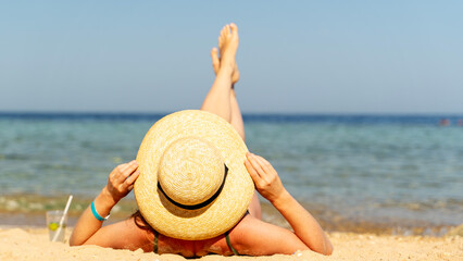 Beautiful woman in a hat sunbathing on the beach by the sea