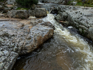 A small stream flows between rugged rocks in a natural landscape, capturing the peaceful movement...