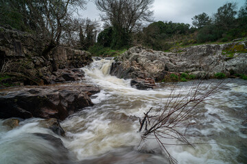 A small stream flows between rugged rocks in a natural landscape, capturing the peaceful movement...