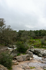 A small stream flows between rugged rocks in a natural landscape, capturing the peaceful movement of water in a wild, untouched environment.