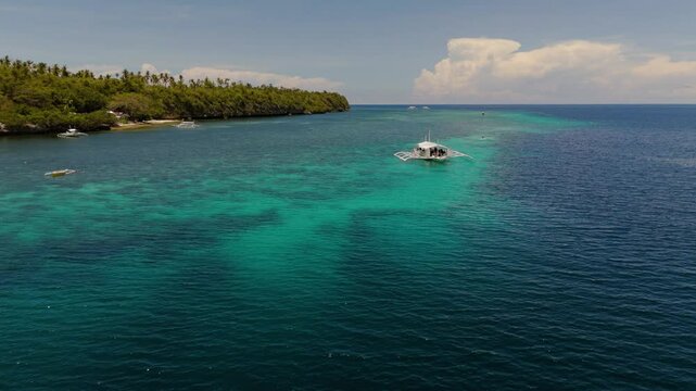 Traditional Bangka Boats and kayaks Near Coral turquoise Waters and tropical palm tree island in Pamilacan Island, Panglao, Bohol, Philippines