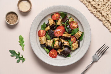 Eggplants tomatoes arugula salad in gray bowl on light beige background. Vegetarian summer Mediterranean salad