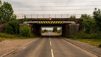 Low bridge crossing under railway bridge with height restriction and warning signs