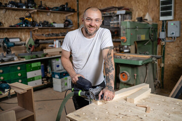 Carpenter working wood with electric planer in workshop