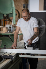 Carpenter using table saw cutting wood plank in workshop