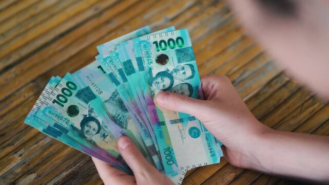 Overhead Shot of a Person Counting and Organizing Stacks of New Philippine 1000 Peso Polymer Banknotes on a Weathered Yellow Wooden Surface &ndash; Focus on Hands and Financial Transaction