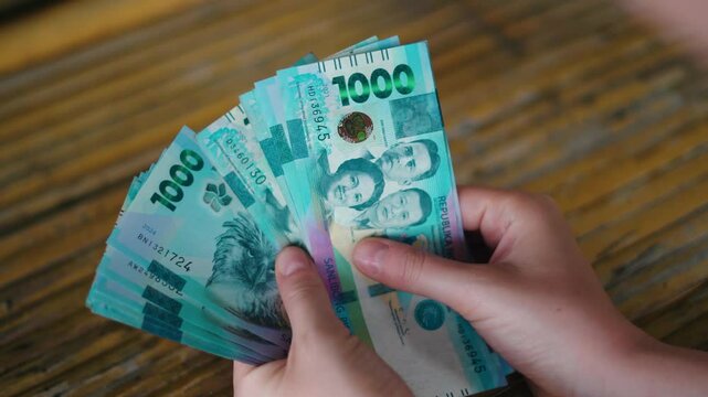 Close-up of a Person Holding and Counting New Philippine 1000 Peso Polymer Banknotes Over a Rustic Wooden Table Surface &ndash; Featuring Hands, Currency Security Details, and Filipino Historical Figures