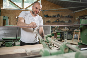 Carpenter sanding wooden plank with belt sander in workshop