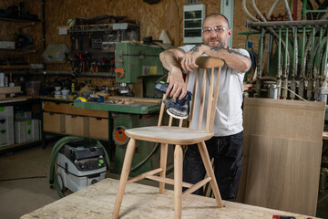 Carpenter sanding wooden chair in workshop with orbital sander