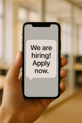 A hand holding a smartphone displaying a hiring advertisement encouraging applications for job opportunities