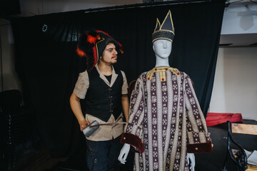 Young performer adjusts a costume displayed on a mannequin in a backstage theater setting,...
