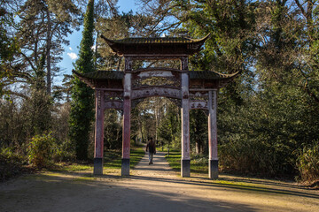 Man walking through the old Chinese gate in the garden of tropical agronomy in Paris. jardin d'argronomie Tropicale Rene-dumont. 