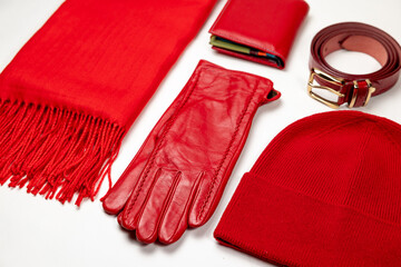 A set of red women's accessories on a white background - a knitted scarf, leather gloves, a knitted hat, a wallet and a belt. The combination of red accessories creates a stylish and bright look