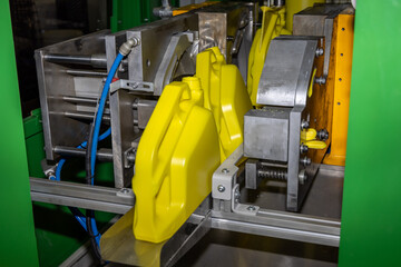 Industrial blow molding machine producing yellow plastic canister. Industrial plastic injection molding process in a factory environment