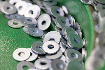 Steel Washers on Vibratory Feeder Track in Industrial Setting. Close-up shot of flat metal washers being oriented on a green vibratory feeder for use in automated assembly. Selected focus