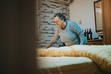 A senior woman arranging the bed linens in a neatly decorated room, featuring warm lighting, brick...