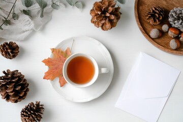 Minimalist seasonal layout with tea, leaves, natural elements and an envelope on white table, perfect for autumn invitations, blogs or social media