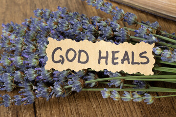 God heals, handwritten quote with lavender on wooden background. Christian biblical concept of...