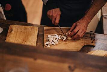 A person uses a knife to slice mushrooms on a wooden cutting board for cooking. The atmosphere is...