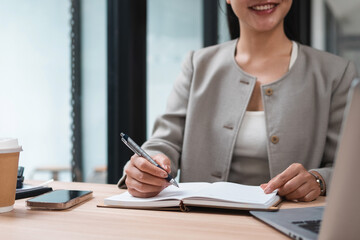 A young woman's hand writing notes in a notebook on a desk.