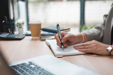 A young woman's hand writing notes in a notebook on a desk.