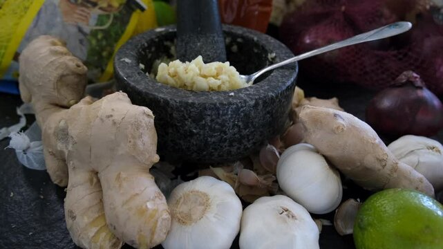 Traditional kitchen setup featuring crushed garlic in a granite mortar, surrounded by ginger roots, onions, and lime &mdash; perfect for cooking or herbal remedies
