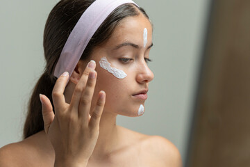 Young woman in profile applying dots of face cream or moisturizer in her beauty routine